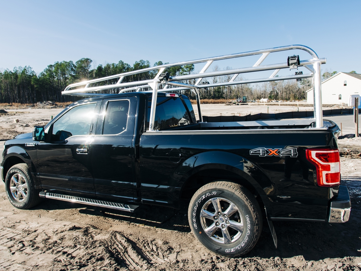 Black Ford F-150 equipped with an aluminum lumber rack at a jobsite.