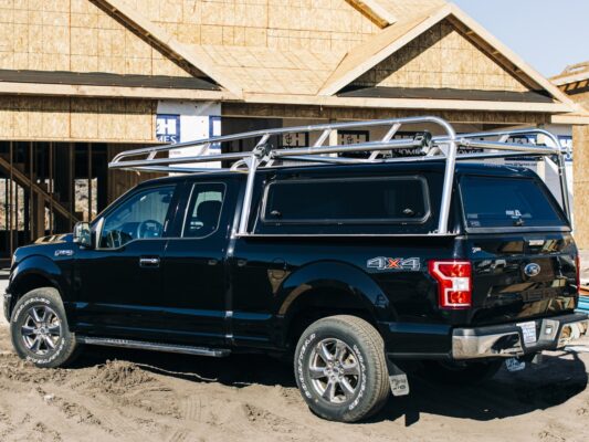 Detailed rear-corner view of a polished aluminum rack fitted to a black Ford F-150 camper shell.