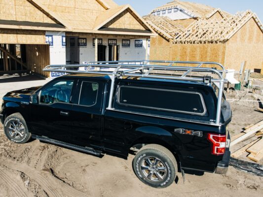 Side view of a polished aluminum rack mounted over a black Ford F-150 topper.