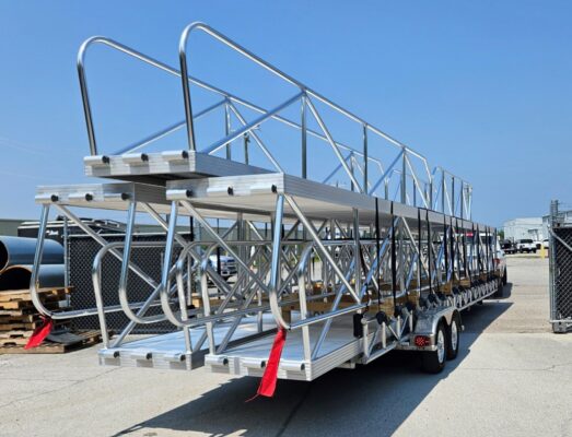 Full‑length trailer carrying built‑to‑order aluminum dock ramps behind a pickup truck