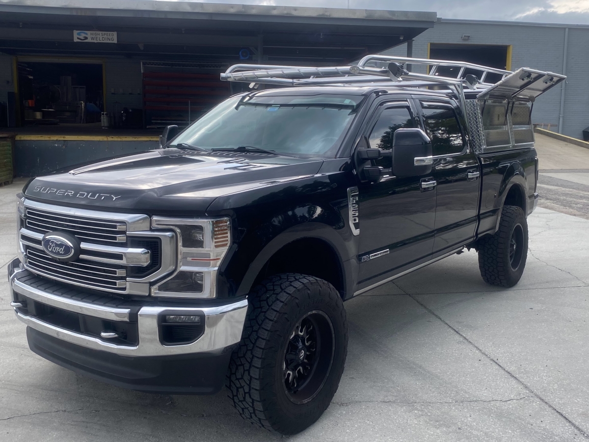 Front three-quarter angle of a black Ford F-250 showing polished aluminum Ryder Rack WELD and diamond-plate Topsider tool boxes.