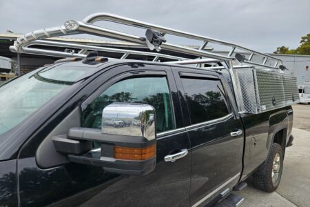 Black pickup truck fitted with Ryder Rack Pro Series ladder rack and XL topsider toolboxes, shown from front-angle view