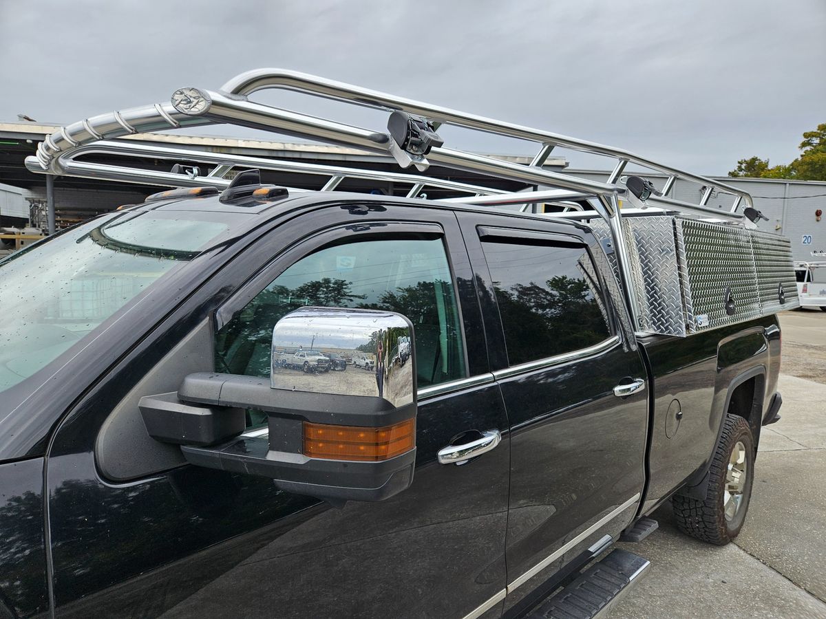 Black pickup truck fitted with Ryder Rack Pro Series ladder rack and XL topsider toolboxes, shown from front-angle view