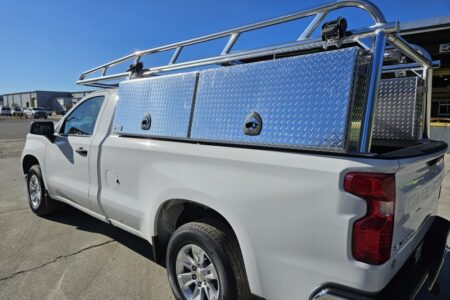Front and side angle of regular‑cab Chevy showing aluminum ladder rack with wind deflectors and topsider toolboxes