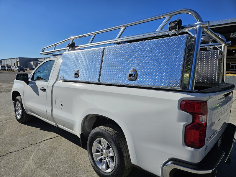 Front and side angle of regular‑cab Chevy showing aluminum ladder rack with wind deflectors and topsider toolboxes